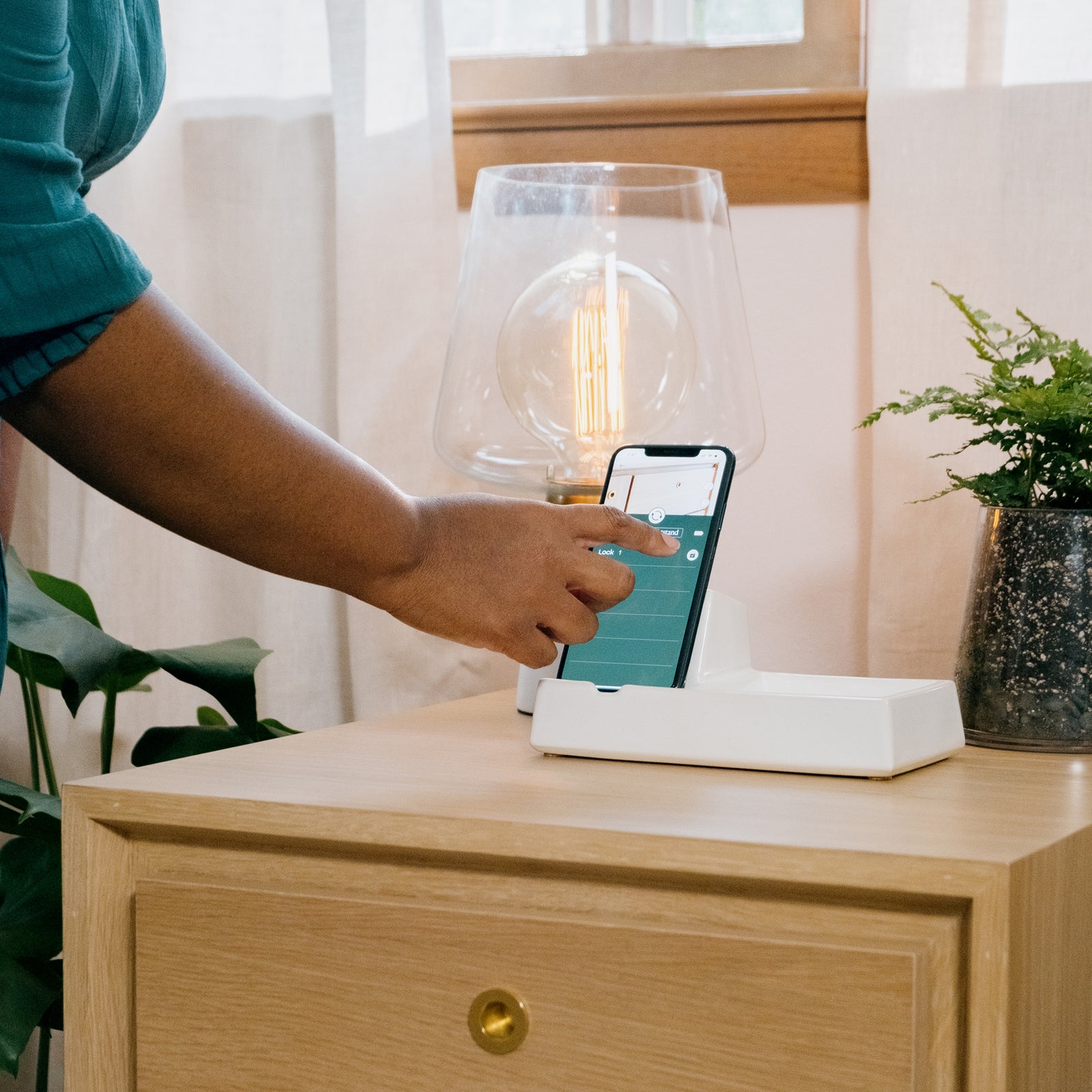 a woman taps the Forti Goods app button to unlock her Grace side table in Oak with clear finish and brass hardware pull.