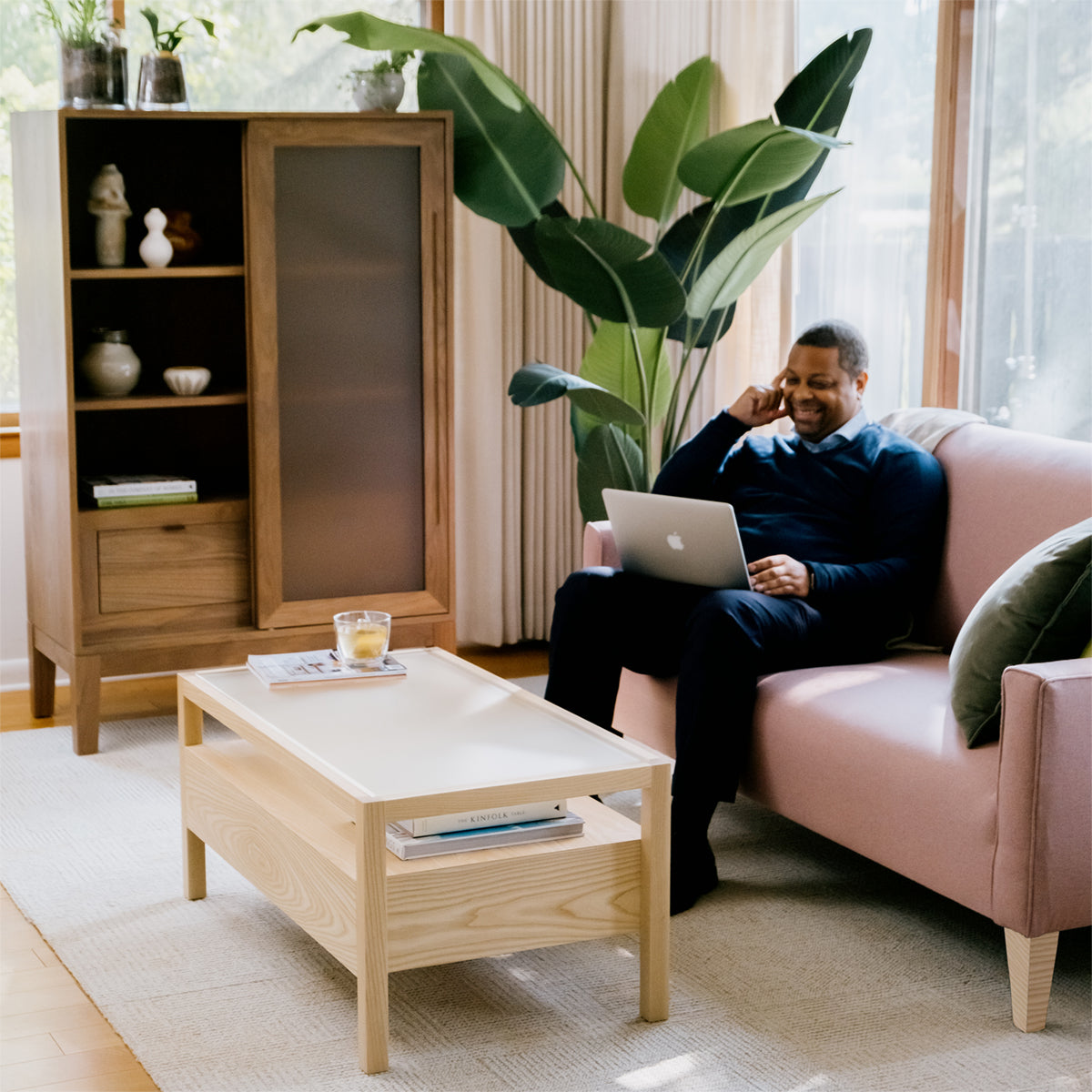 a man sitting on a sofa looking at his laptop with a cup of tea on his Forti Goods Sylvia locking coffee table and next to his Geraldine locking drawer cabinet in walnut.